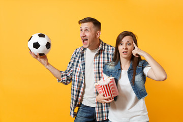 Wall Mural - Young fun cheerful couple, woman man, football fans holding soccer ball, bucket of popcorn, cheer up support favorite team, isolated on yellow background. Sport play family leisure lifestyle concept.