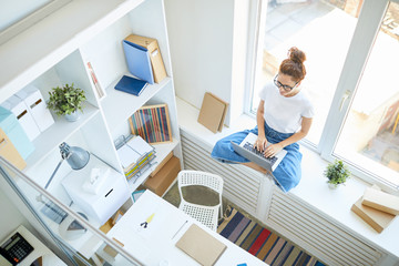 Canvas Print - Young office manager with crossed legs sitting on window-sill and working in the net