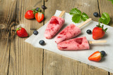 Świeże domowej roboty lody truskawkowe na patyku na drewnianym tle. 
