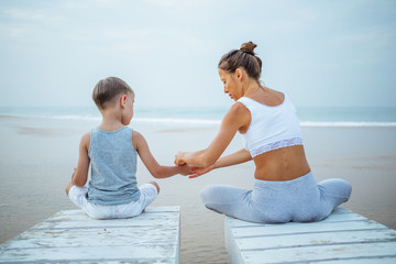 Wall Mural - A mother and a son are doing yoga exercises at the seashore of tropic ocean