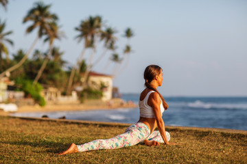 Caucasian woman practicing yoga at seashore of tropic ocean