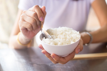 Hand of a woman holding a scoop of  white rice in the bowl.