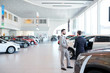 Professional salesperson selling new cars in a modern auto salon. Two men standing and choosing a new car