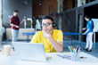© Seventyfour - Portrait of  creative young Middle-Eastern man wearing glasses and bright yellow shirt using laptop while working in open space office of IT developers team, copy space