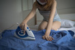 © NopponPAT - oung woman with iron ironing man blue shirt during housework. Female ironing clothes on white bed.  Blue iron on white bed.