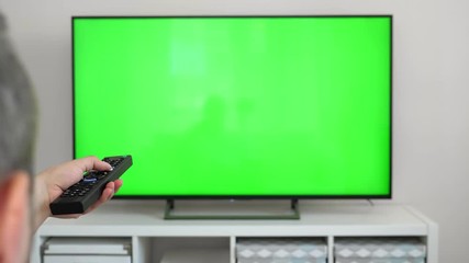 Watching tv with green screen at home interior. Push buttons on remote