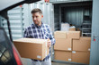 © pressmaster - Serious handsome young man in casual clothing finding place in car for cardboard box while loading automobile at container storage area, he storing things in container