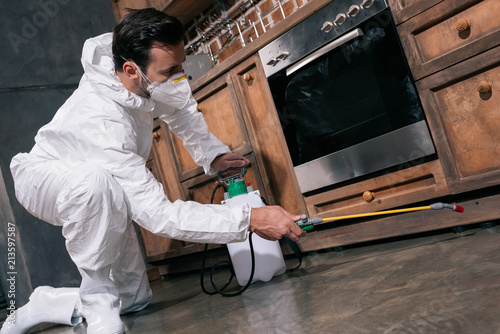 Fotografía pest control worker spraying pesticides under cabinet in kitchen