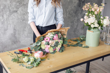 Woman florist creating beautiful bouquet in flower shop. Working in flower shop. Girl assistant or owner in floral design studio, making decorations and arrangements.