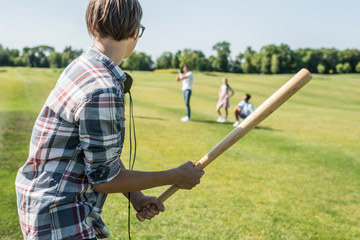 Wall Mural - side view of teenage boy holding baseball bat and playing with friends in park