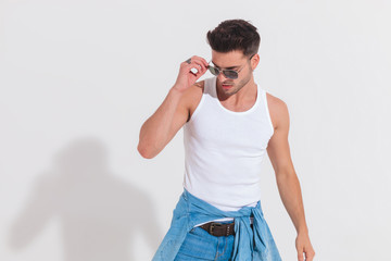 Wall Mural - casual man in studio light fixes sunglasses and looks down