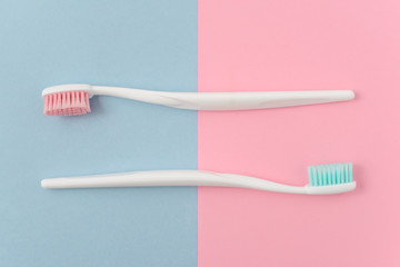 Close up of two plastic white toothbrushes with pink and blue bristle on pink and blue background. Free copy space.