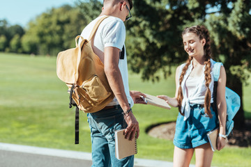 Wall Mural - smiling teenage boy and girl holding book together in park