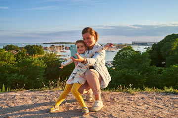 Young mother and her daughter taking a selfie, sea on background, Kaivopuisto park, Helsinki, Finland