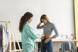 © Anton - Beautiful fashion designer thoughtfully measuring customer with tape while working in modern sewing workshop