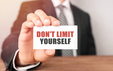 Poster - businessman holding a card with text don't limit yourself