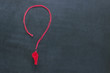 Sports whistle on a red lace. It is laid out in the form of a question mark. Concept- sport competition, referee, statistics, challenge, friendly match.Copy space.