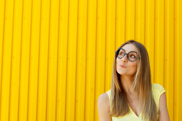 Wall Mural - Portrait of a thoughtful girl wearing toy funny glasses looking up over yellow background at daylight