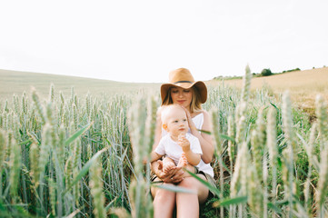 a young mother and her little child sitting near the wheat on a green background