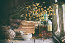 Mortar Of Dried Healing Herbs, Bottle Of Essential Oil Or Infusion, Old Books And Bunch Of Dry Chamomile Plant. Herbal Medicine.