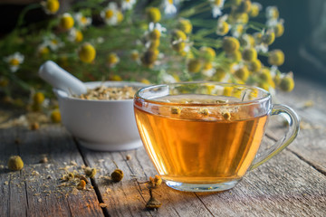 Healthy chamomile tea or infusion, mortar and daisy herbs on wooden board.