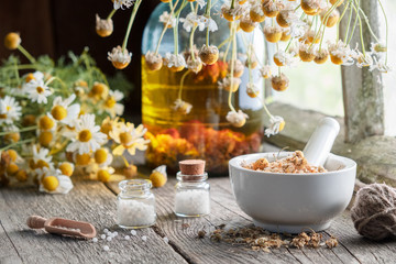 Wall Mural - Mortar of dried healing herbs, homeopathic globules, bottle of oil or infusion and bunches of dry chamomile plant. Homeopathy and herbal medicine.