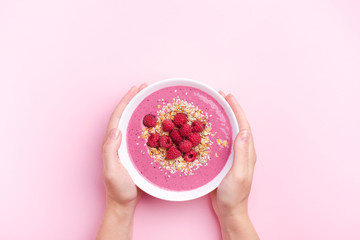 Wall Mural - Woman's hands holding raspberries smoothie bowl on pink background. Top view, copy space.