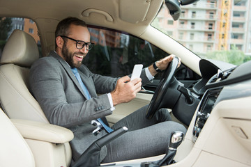 handsome smiling man using smartphone while driving car