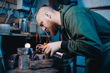 Smith jeweler produces silver metal smelting, holds gas burners in his hand.