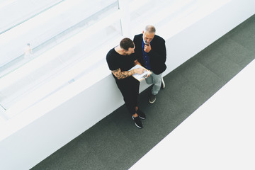 View from the top photo of two businessmen discussing business points of the upcoming meeting with the investors. Office employees sharing ideas for the new project while having informal meeting.