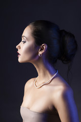 Wall Mural - Beautiful brunette girl with naked shoulders and dark red lips make-up, wearing earrings and a pearl necklace, illuminated in blue.