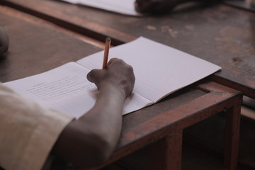 african education - close up of a school kid sitting inside a classroom, holding a pencil, indoors on a sunny day