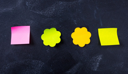 Sticky colorful notes in flower and square shapes, isolated, copy space on blackboard background.