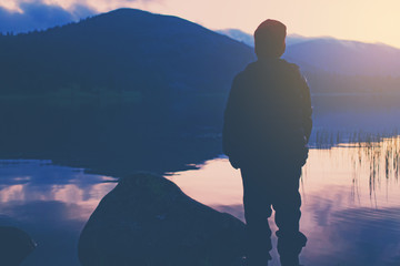 The silhouette behind the young boy at sunset on the shore of a mountain lake