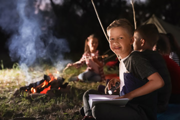 Wall Mural - little boy with book and flashlight near bonfire at night. summer camp