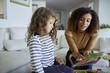 © Cavan Images - Mother reading picture book for daughter while sitting on sofa at home
