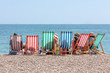 Rear View of Group of People Seated in Six Striped Deckchairs at the Seaside on a Bright Sunny Summer Day