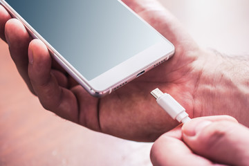 Plugging In A White USB Cable In A White Smartphone By Male Hands