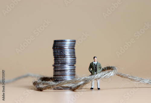 Fotomural A miniature man connected with a pile of coins and rope.