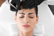 Young woman undergoing procedure of eyebrow permanent makeup in beauty salon