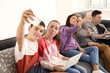 © Africa Studio - Group of teenagers with modern devices taking selfie while sitting on sofa indoors