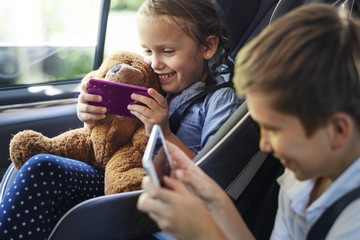 Sister and brother playing with digital devices in the car