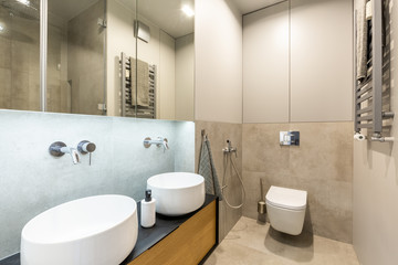 Stylish, modern ensuite bathroom interior with beige marble tiles, big mirror and two washbasins for a couple