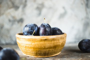 Wall Mural - Ripe blue plums in a clay bowl on a gray table. Summer seasonal fruit concept