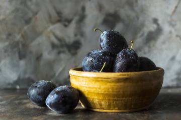 Wall Mural - Ripe blue plums in a clay bowl on a gray table. Summer seasonal fruit concept