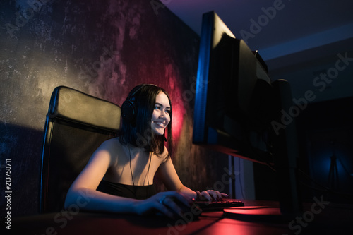 Fotografie, Obraz A cute female gamer girl sits in a cozy room behind a computer and plays games