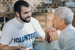 © Viacheslav Yakobchuk - I trust you. Attractive cheerful bearded volunteer smiling and talking with an old man while sitting in the kitchen