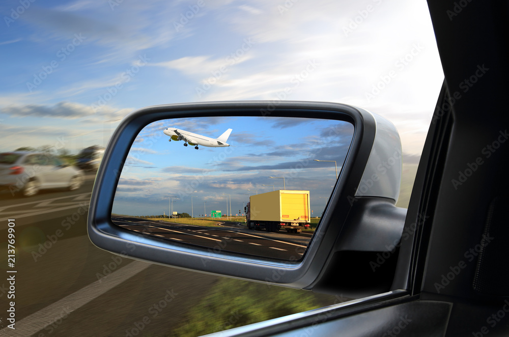 Widok w lusterku samochodu osobowego jak samolot wznosi sią nad ciężarówką . - obrazy, fototapety, plakaty 