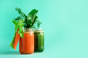 Wall Mural - Healthy organic green and orange smoothies on blue background. Detox drinks in glass jar from vegetables - carrot, celery, beet greens and tops. Copy space. Summer food concept