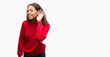 Young hispanic woman wearing red sweater smiling with hand over ear listening an hearing to rumor or gossip. Deafness concept.